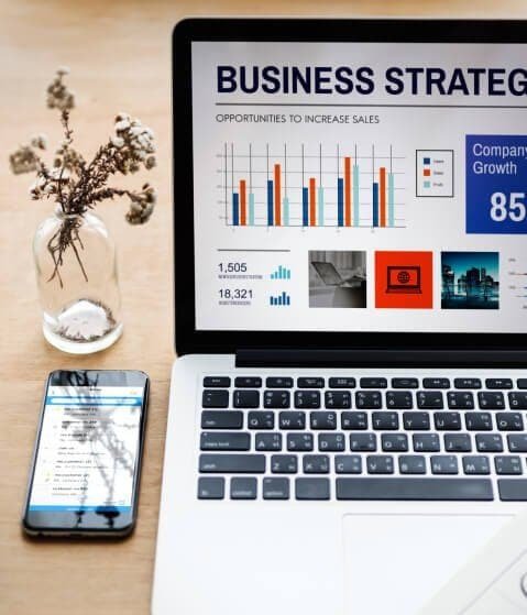 Business strategy analysis with charts on a laptop and a smartphone on a desk.